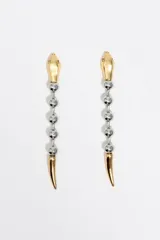 Caravanas largas con diseño de serpiente en acabado bicolor dorado y plateado. Presentan una cabeza dorada en la parte superior, un cuerpo formado por esferas plateadas y una cola puntiaguda dorada en el extremo inferior. Cuentan con cierre de presión.