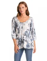Blusa de tejido estampado con diseño floral en tonos grises y blancos, con escote redondo decorado con aplique de encaje y mangas tres cuartos tipo raglán.