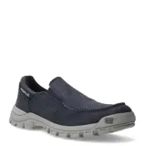 Zapatos tipo slip-on de la marca Caterpillar, confeccionados en lona de color azul marino. Presentan un diseño de estilo casual con costuras reforzadas en la puntera, elásticos laterales para un calce fácil y una suela de goma robusta en color gris con el logo de la marca en el lateral.