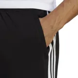 Pantalón de training Adidas color negro, corte clásico con perneras ajustadas en el puño. Presenta cintura elástica con cordón ajustable, bolsillos laterales con cremallera y tres franjas blancas verticales a lo largo de las costuras laterales.
