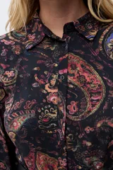 Vestido midi de corte camisero con estampado paisley en tonos oscuros, manga larga con puños ajustados y cierre frontal de botones. Presenta un diseño fluido con falda de volantes en el ruedo.