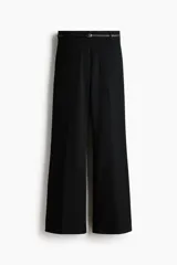 Pantalón de tiro alto y piernas acampanadas color negro, con bolsillos tipo parche en el frente, pliegues planchados al frente y en la espalda, y un cinturón fino incluido.