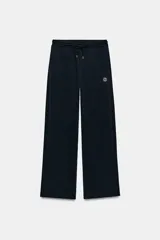 Pantalón tipo jogger de tiro medio con cintura elástica ajustable mediante cordones. Presenta un diseño de pierna recta, bolsillos laterales ocultos en las costuras y un detalle metálico con el logo ZA en la parte superior.