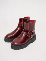 Bota corta de cuero negro tipo biker, con suela track de goma, plataforma, costuras y bordados decorativos en hilo rojo. Presenta tiras con hebillas metálicas y cierre en la parte trasera.