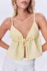 Top amarillo pálido con escote en V, breteles finos con lazos en los hombros y corte holgado con frunce y lazo ajustable en el centro del busto.
