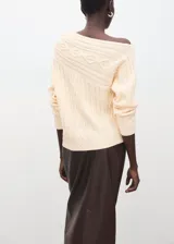 Sweater de punto color beige, con diseño de ochos, cuello bote drapeado y manga larga.