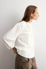 Blusa blanca de corte holgado con cuello mao y escote en V. Presenta detalles de bordado calado en el pecho y en los puños de las mangas tres cuartos.