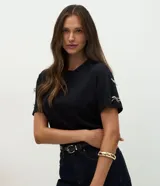 Remera básica de algodón color negro, con cuello redondo, manga corta y detalles de moños brillantes aplicados en las mangas.