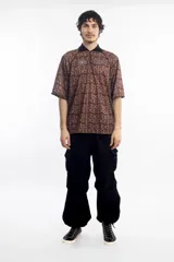 Remera deportiva marrón con cuello polo negro, cierre parcial con cremallera, mangas cortas y estampado con letras.