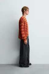 Jersey relaxed fit de punto calado con rayas horizontales en tonos naranja y amarillo. Tiene cuello redondo y manga larga con acabados irregulares.