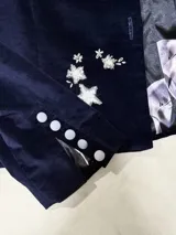 Chaqueta de paño de lana y cashmere color verde oscuro, de corte estructurado con cuello mao, mangas largas con hombros abullonados y puños con tajo. Cuenta con cierre frontal de botones dorados grandes y detalles de bordados dorados artesanales en el pecho y el bajo.
