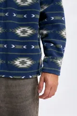 Sobrecamisa de tejido polar con estampa abstracta en tonos azules, verdes y blancos. Presenta cuello camisero, cierre frontal con botones, dos bolsillos frontales con solapa y botones, y un interior afelpado para mayor abrigo.
