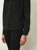Camisa de jean de corte recto con cuello alto tipo mao con volados, cierre frontal con botones a presión y mangas largas con hombros ligeramente abullonados.