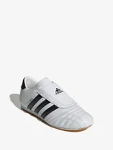 Zapatillas Adidas Taekwondo blancas con las tres tiras negras y suela de goma color caramelo.