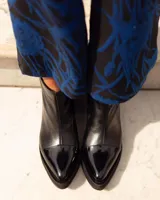 Botinetas de cuero negro con diseño de punta fina en charol brillante y suela de plataforma. Presentan una costura central vertical en el empeine.