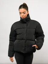 Campera puffer corta Umbro de color negro, con cuello alto, cierre frontal y bolsillos laterales. Presenta un diseño acolchado y logo de la marca bordado en el pecho.