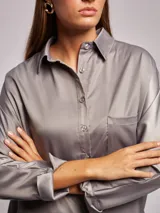 Camisa gris de corte amplio, con cuello solapa, escote en pico y manga larga.