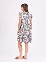 Vestido corto de corte holgado con estampado floral en tonos blancos y naranjas sobre base gris oscuro. Presenta escote en V, mangas con volados y diseño escalonado.