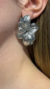 Caravanas de diseño floral con acabado metálico plateado y textura estriada que simula los pétalos de una flor.