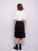 Falda midi de jean color negro, con diseño de cinco bolsillos, cierre frontal con botón metálico y abertura central en el bajo.