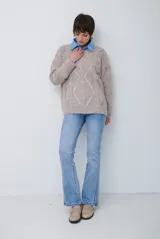 Buzo de punto color beige con diseño de trenzas y costuras decorativas en contraste que forman rombos. Presenta cuello redondo, mangas largas y puños acanalados.