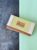 Billetera de cuero color camel con solapa verde lima y detalles en color crema. Tiene cierre con broche y monedero externo.
