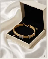 Pulsera de plata 925 con baño de oro, compuesta por una cadena de malla metálica y dijes decorativos, incluyendo una mariposa central con incrustaciones de circonias.