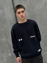 Buzo negro de corte holgado con cuello redondo y puños y bajo acanalados. Estampado frontal con un sol y la palabra "Osten" en blanco.