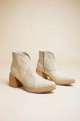 Botas cortas de cuero color crema, con puntera fina, paneles laterales con textura de piel de reptil, cierre lateral con cremallera y tacón geométrico de madera.