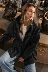 Campera tipo overshirt de paño jaspeado en color negro, con calce oversize, capucha y cordones trenzados. Presenta un diseño versátil con interior suave y abrigado.