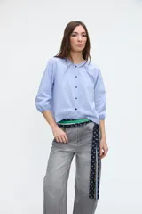 Camisa de manga larga con diseño a rayas celestes y blancas, cuello redondo y cartera de botones frontales. Presenta mangas con puños elásticos.