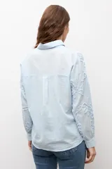 Camisa celeste con apliques florales bordados, cuello camisero, manga larga y cierre frontal de botones.