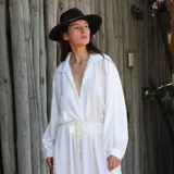 Camisa de crepé color blanco, con cuello solapa, escote en V profundo y mangas largas abullonadas con puños ajustados. Presenta un diseño holgado con cintura elástica y cordón ajustable.
