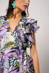 Vestido largo con estampado floral en tonos lila, verde y negro. Tiene escote en V, mangas cortas con volados y corte cruzado con lazo en la cintura.