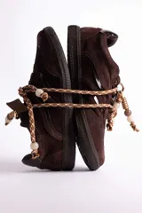 Zapatillas urbanas de gamuza color marrón, con diseño de cordones decorados con cuentas de piedra y detalles de líneas brillantes en los laterales. Presentan suela de goma texturizada al tono.