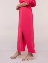 Vestido largo amarillo de corte fluido con escote en V, mangas cortas amplias y apliques de tachas en el escote y puños. Posee cintura elastizada fruncida y falda larga con tajos laterales en el ruedo.