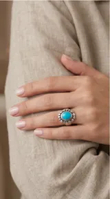Anillo de plata 925 con piedra central ovalada de pasta de turquesa y diseño de borde texturizado con detalles circulares.