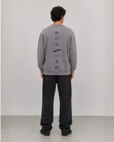 Buzo oversize de cuello redondo en color gris, con diseño estampado en el frente que incluye logotipos y texto. Presenta puños y ruedo acanalados, con una pequeña etiqueta decorativa en la parte inferior.