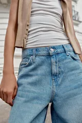 Jeans baggy de tiro medio con pernera holgada, diseño de cinco bolsillos y bajo acabado en vuelta. Cuenta con cintura elástica en la espalda y cierre frontal con cremallera y botón.