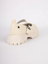 Zapatos tipo guillerminas color crudo, de tela, con correa ajustable y hebilla metálica. Cuentan con plataforma de 4,5cm.