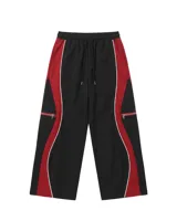 Pantalón deportivo oversize de corte amplio, color negro con paneles laterales rojos y ribetes blancos. Cuenta con cintura elástica con cordón ajustable y bolsillos laterales con cierre.