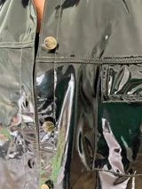 Camisa negra de charol con cuello clásico, cierre frontal con botones y bolsillos de parche en el pecho.