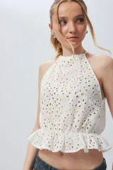 Top blanco sin mangas con cuello halter, bordado con calados y elástico con volado en la cintura.