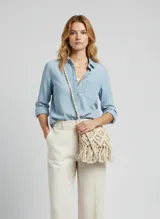 Cartera bandolera de crochet color beige claro, con diseño de rombos y flecos en el borde inferior. Posee solapa y correa larga trenzada.