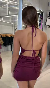 Vestido corto bordó satinado con escote halter fruncido, espalda descubierta y falda ajustada con frunces laterales.