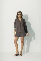 Camisa de corte relajado con diseño de rayas verticales en tonos rojos, marrones y blancos. Presenta cuello clásico, cierre frontal con botones al tono y mangas largas con puños que permiten un estilo arremangado.