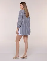 Blusa de silueta holgada a rayas verdes y blancas, confeccionada en tela liviana con textura arrugada. Presenta cuello en V profundo con botones frontales, mangas 3/4 de hombro caído y ruedo asimétrico con aberturas laterales.