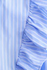 Blusa cruzada celeste a rayas blancas de popelina de algodón, con escote en V pronunciado, mangas cortas abullonadas, volados en el frente y detalle de lazo para atar en la cintura.