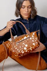 Cartera tipo bolso de mano confeccionada en cuero gamuzado color suela, con solapa de cuero liso y cierre metálico. Incluye doble manija corta y correa larga desmontable.