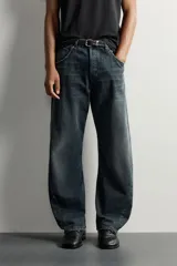 Jeans loose fit de hombre en denim de algodón color gris oscuro con efecto lavado. Presenta perneras con costuras giradas hacia los tobillos, tiro medio, cierre frontal con botones y bolsillos frontales con bolsillo cerillero.